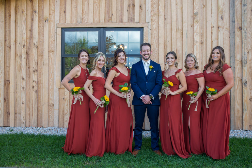 groom with bridesmaids at wedding rings on a sunflower bouquet at fall wedding at the barn