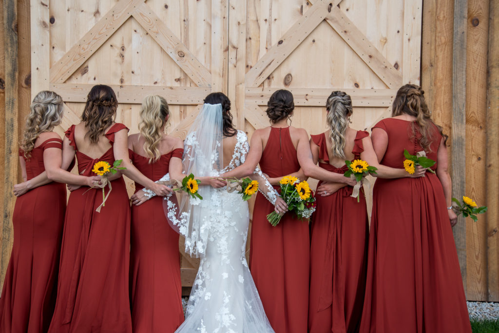 bride with her girls at wedding rings on a sunflower bouquet at fall wedding at the barn