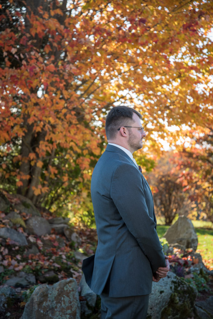 groom standing in front of a beautiful orange fall tree waiting for the first look at the perfect fall wedding