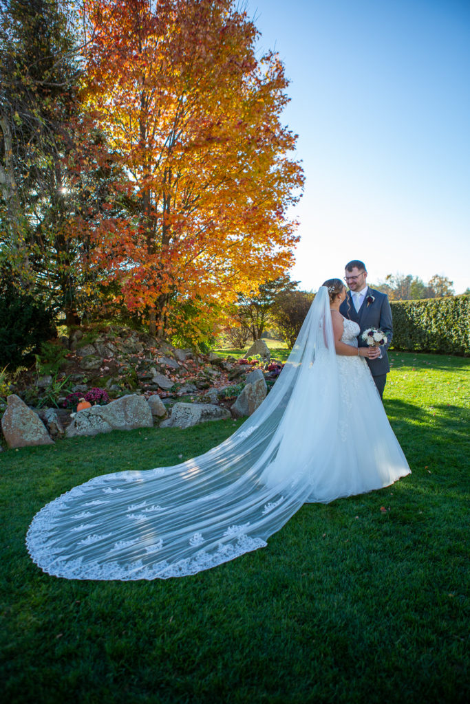 bride and groom by a fountain and beautiful orange foliage tree at the perfect fall wedding