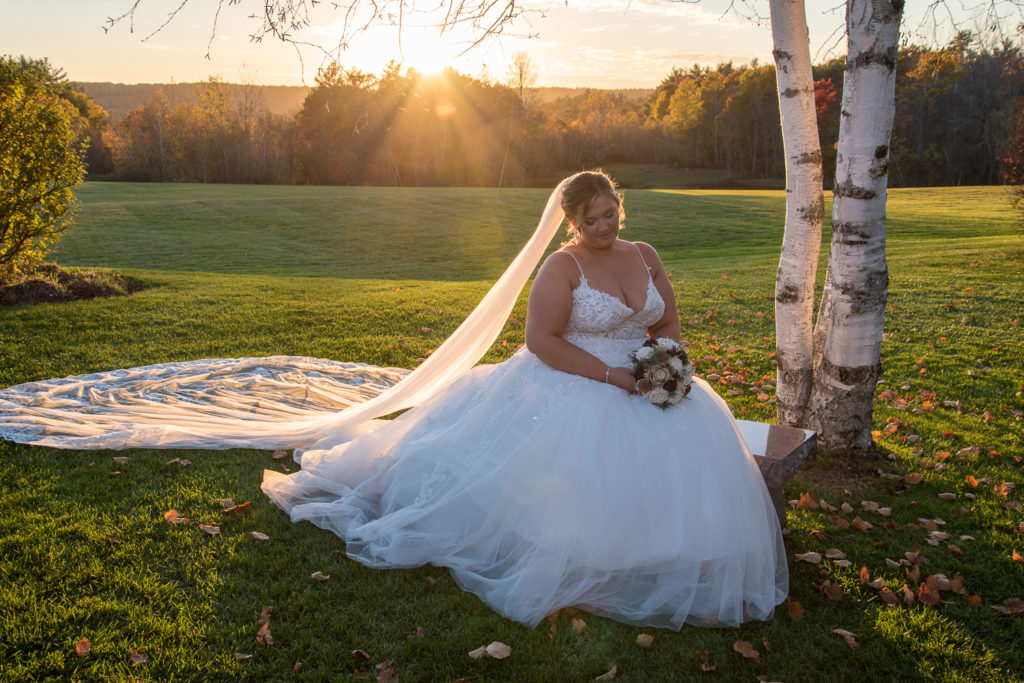 bride sitting on a bench in front of the perfect fall wedding sunset