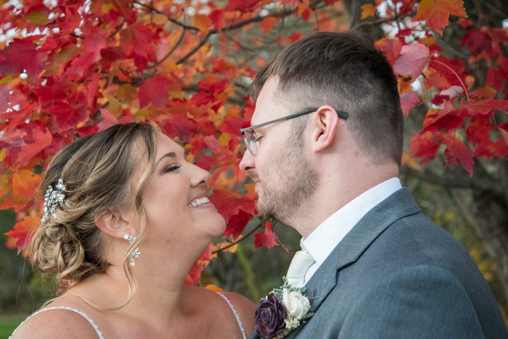 bride and groom in front of a red foliage tree at the perfect fall wedding 