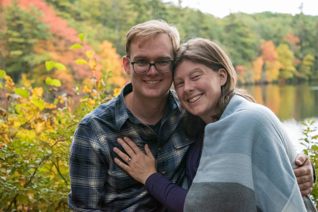 Best of 2021 Engagement bride and groom to be snuggling with fall foliage behind them