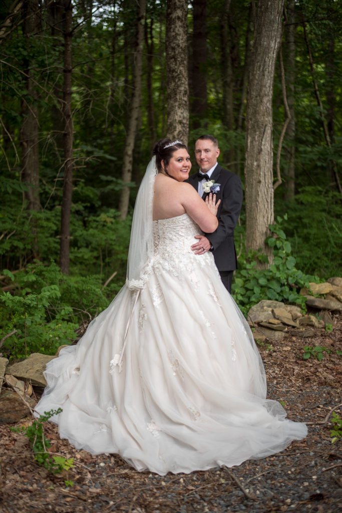 bride and groom hugging and smiling at the camera with the woods behind them - 2021 wedding