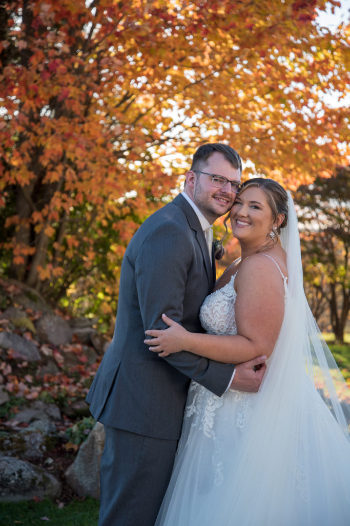 Bride and groom hugging in front of an orange autumn tree fall 2021 wedding