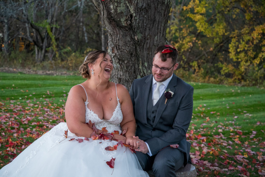 bride and groom laughing with red fall leaves on them 2021 weddings 