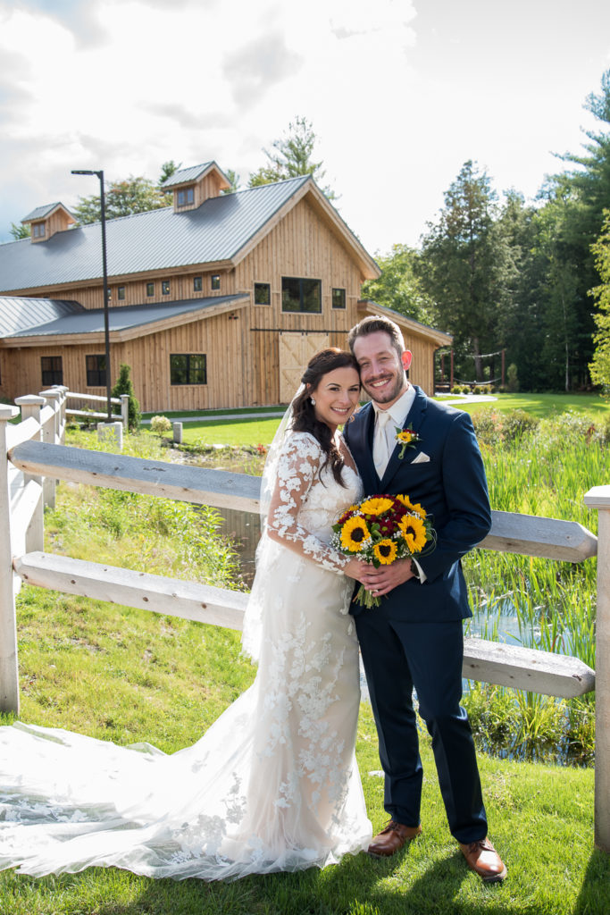 bride and groom posing in front of the Barn at Bull Meadow and white fence 2021 fall wedding