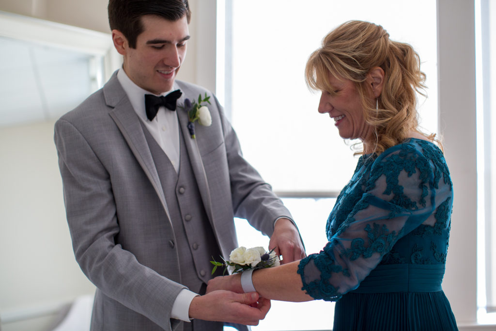 groom putting his mom's corsage on at winter oceanside wedding 