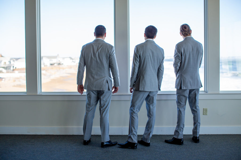 groom with his groomsmen looking out the window at the ocean at winter oceanside wedding 