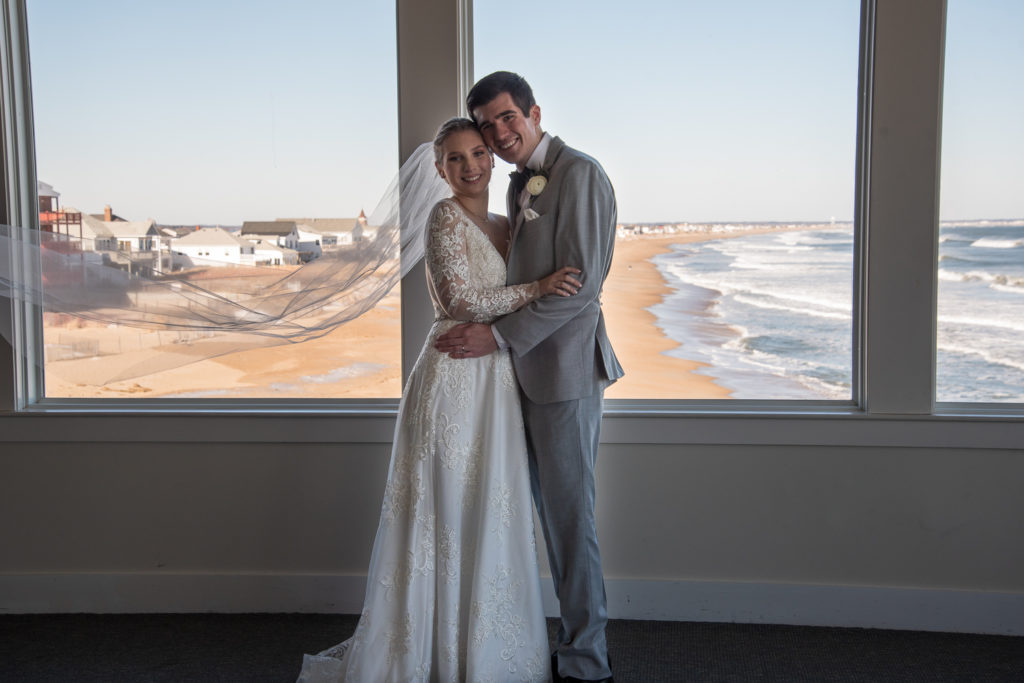 bride and groom hugging with the ocean in the background out the windows. veil flying in the air