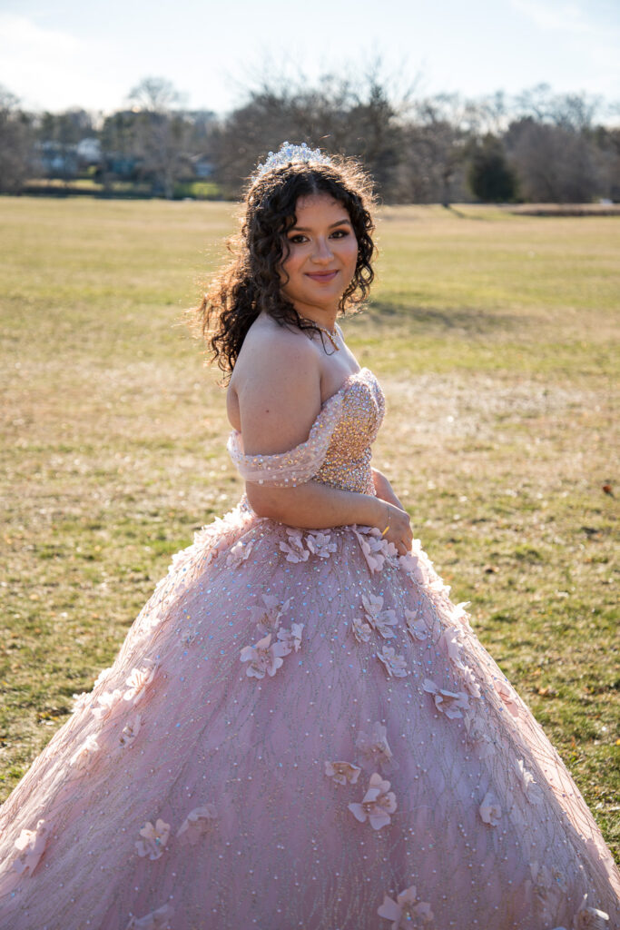 Sweet 16 birthday girl posing in a big pink ballgown at a park