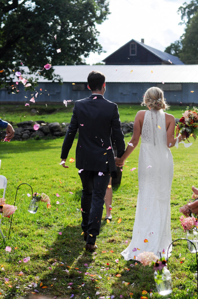 bride and groom leaving ceremony site, flower petals in the air