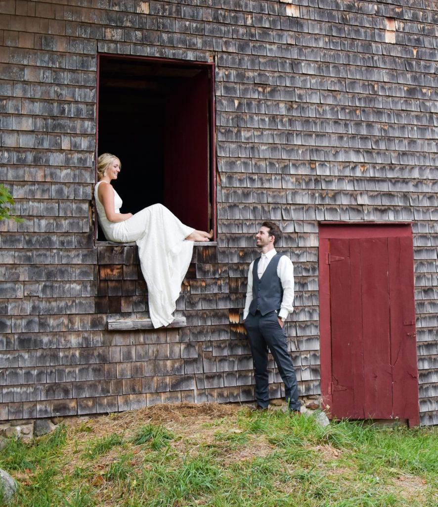 bride sitting in upper doorway of the barn and groom on the ground looking up at her