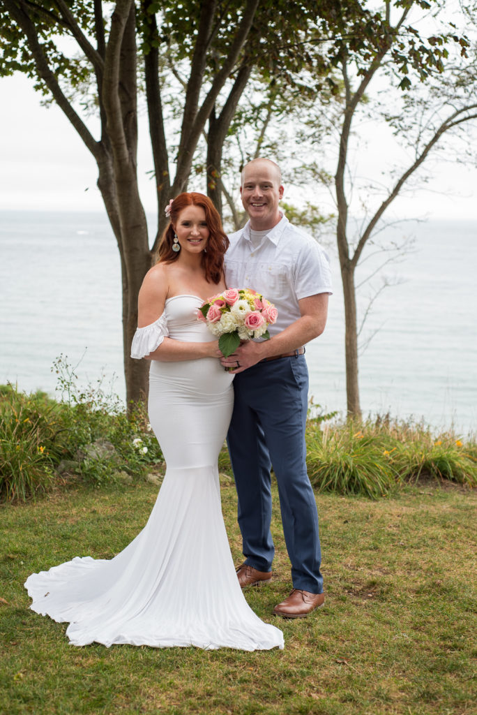bride and groom smiling at the camera with ocean in the background