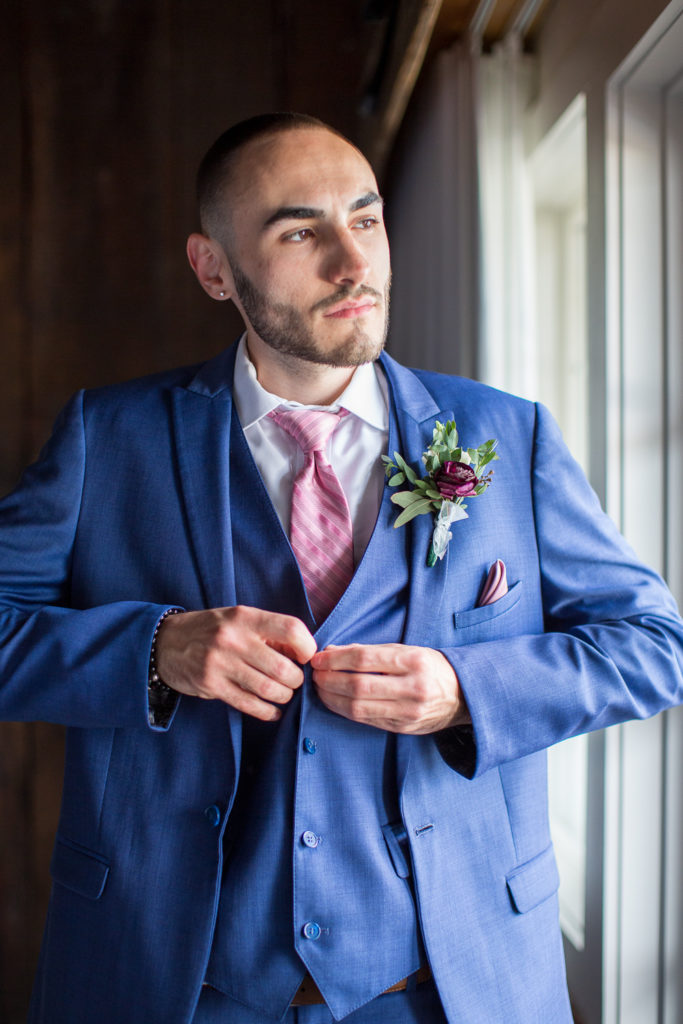 groom buttoning his vest while looking out the window