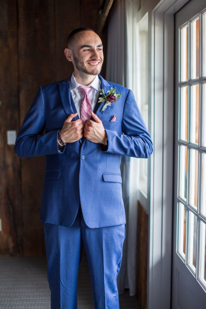 groom smiling while looking out the window, holding his jacket