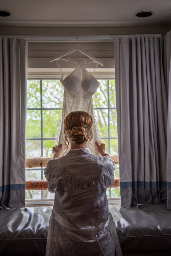 Bride looking at her dress hanging up in the window