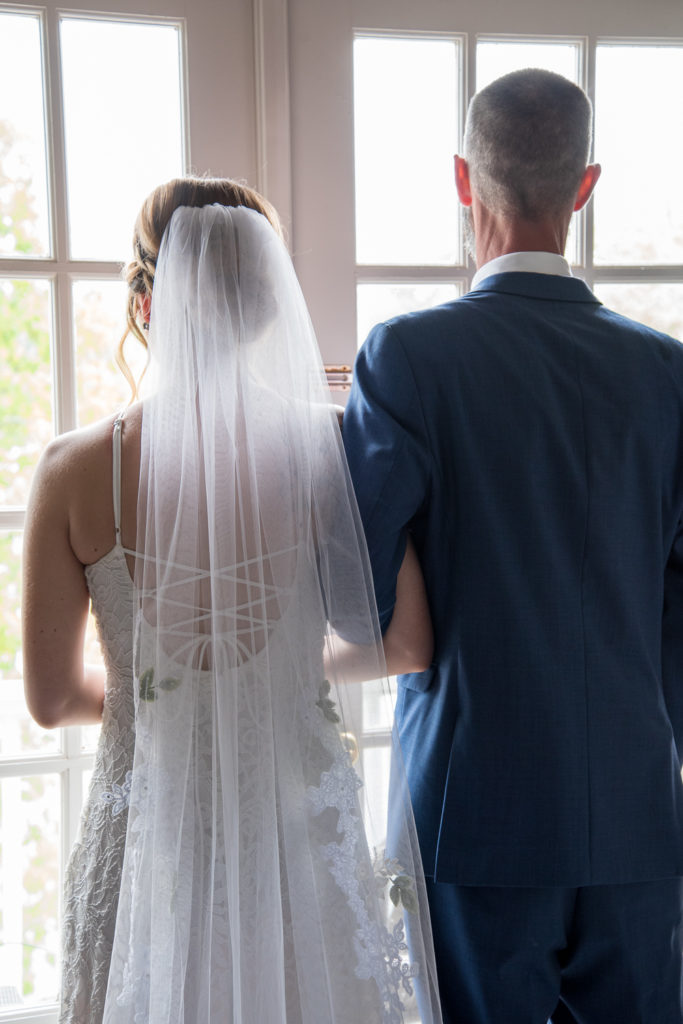 bride and her dad looking out of french doors, linked arms