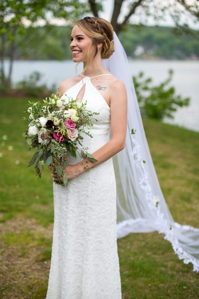 bride posing in front of the lake with her veil and bouquet