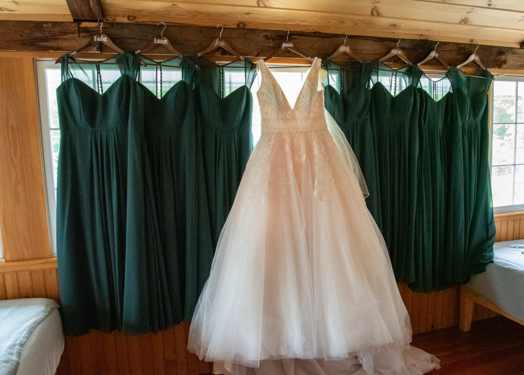 bride's dress hanging in the window with all the bridesmaids emerald green dresses on either side