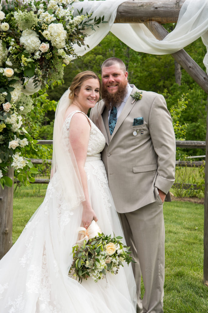 Bride and groom posing in front of their beautiful, magical rustic elegant arbor with florals 