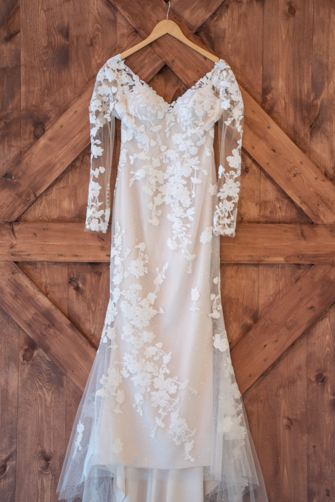 wedding dress hanging in front of barn door at fall wedding at the barn