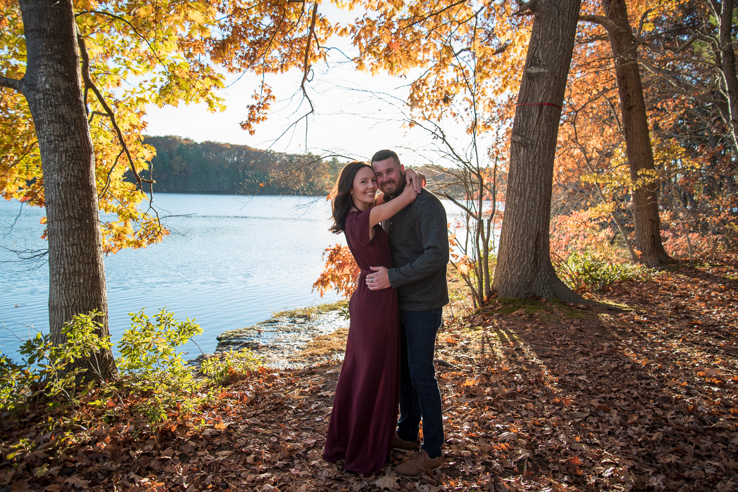 bride and groom to be hugging with the ocean behind them and fall foliage