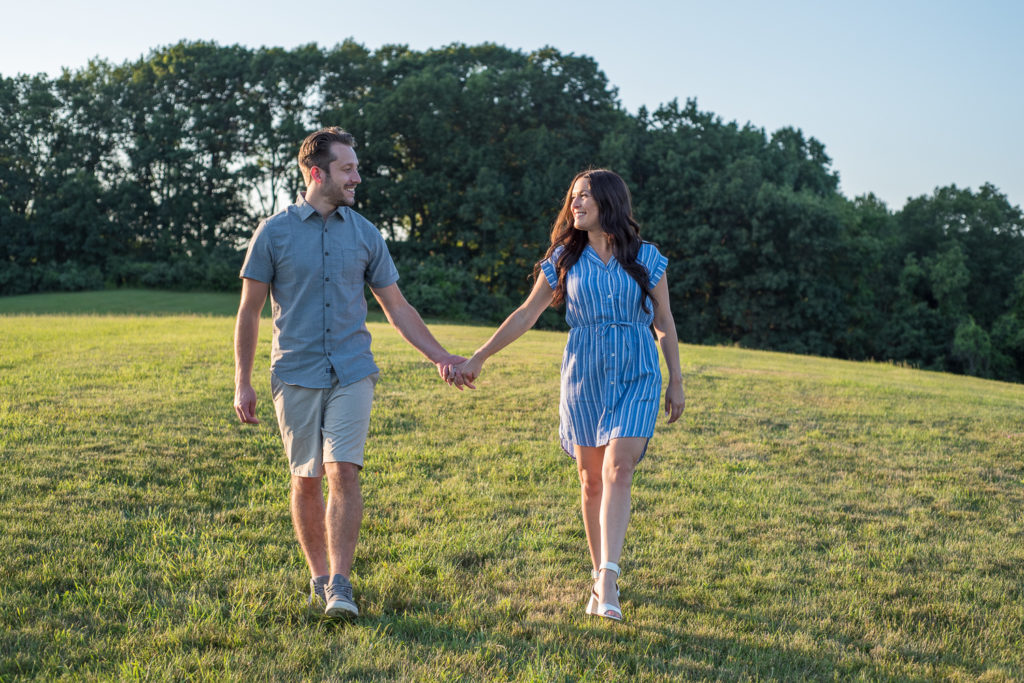 couple walking holding hands during engagement session in field