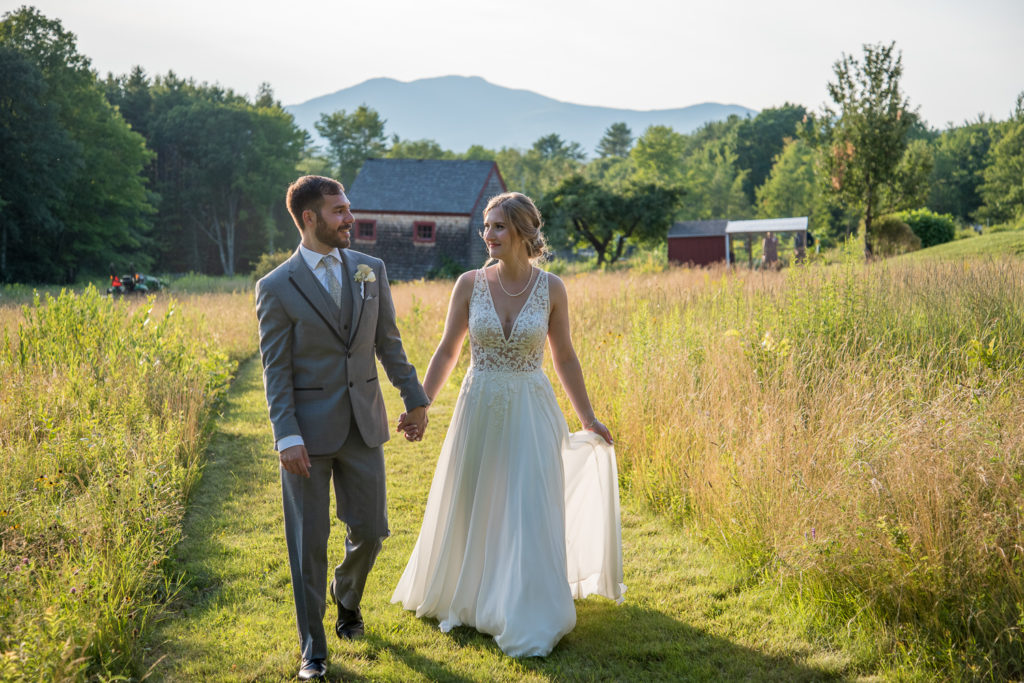 bride and groom walking hand in hand in a field with the mountains behind them - 2021 wedding