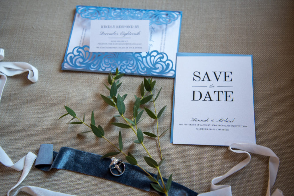 details shot for Winter Oceanside wedding with invites, greenery, wedding rings and ribbon