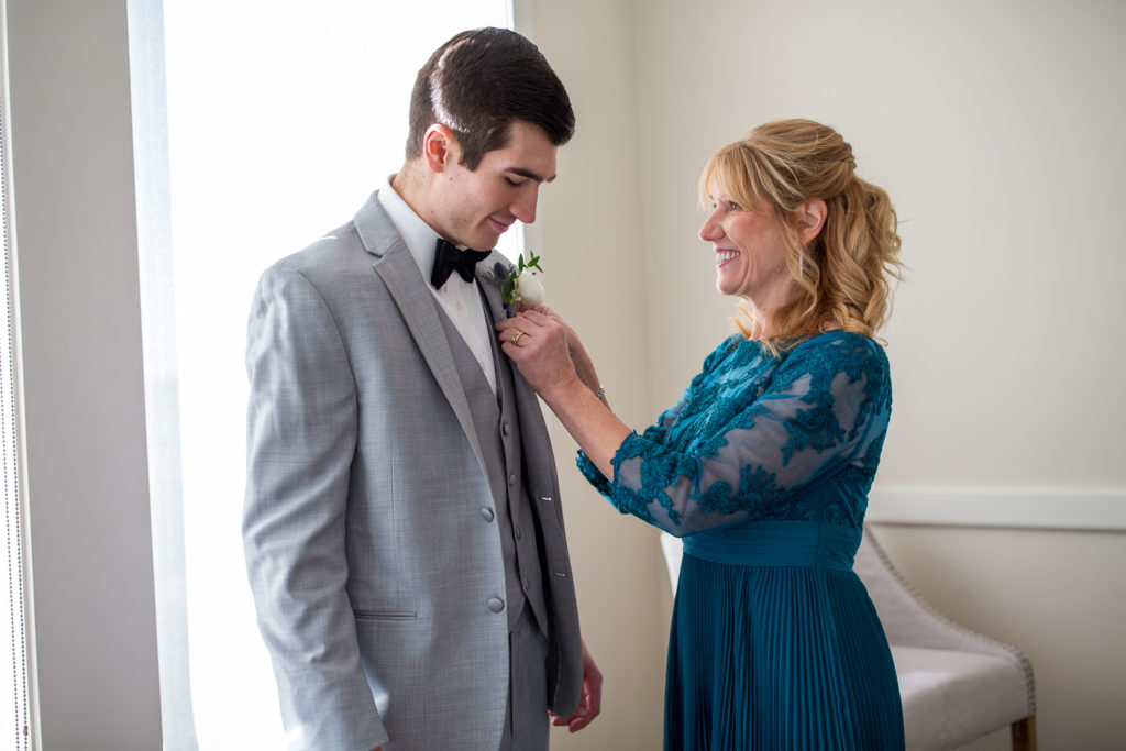mother of groom putting on groom's boutonnière at winter oceanside wedding 