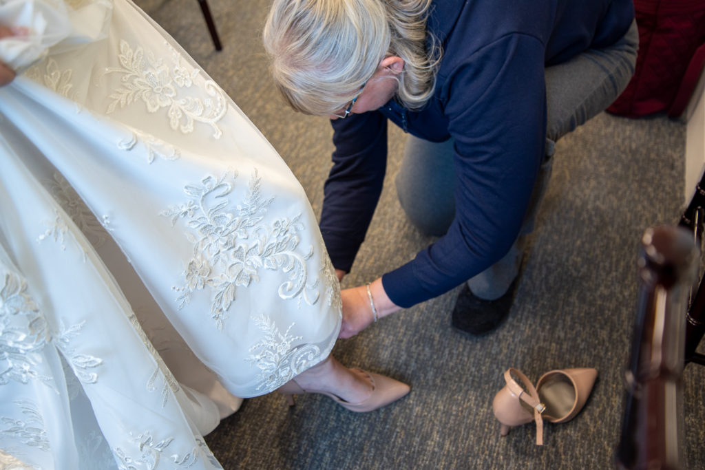 mother of bride putting on bride's shoes at winter oceanside wedding 