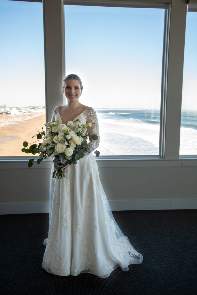 bride smiling in front of windows with ocean in the background at winter oceanside wedding 