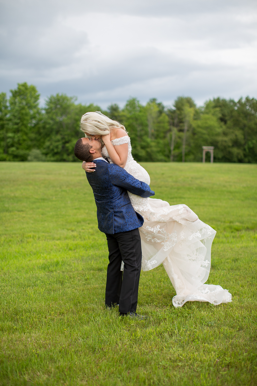 groom picking up his bride in a field 