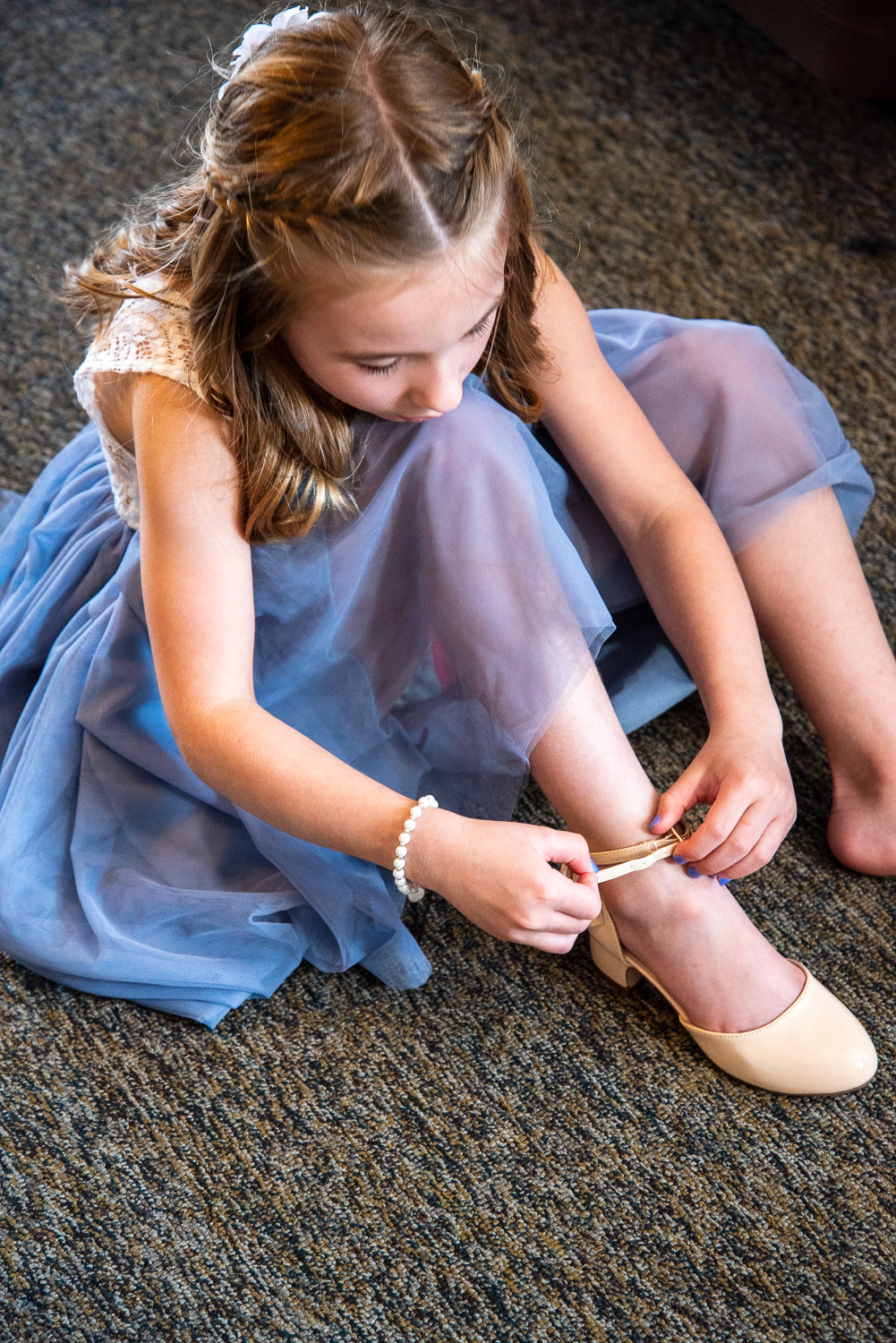 Flower girl putting shoes on before the lakeside wedding