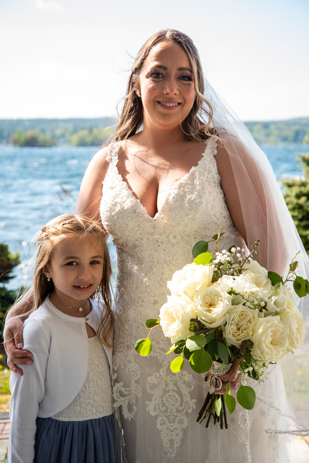 Bride holding bouquet standing with the flower girl after the lakeside wedding