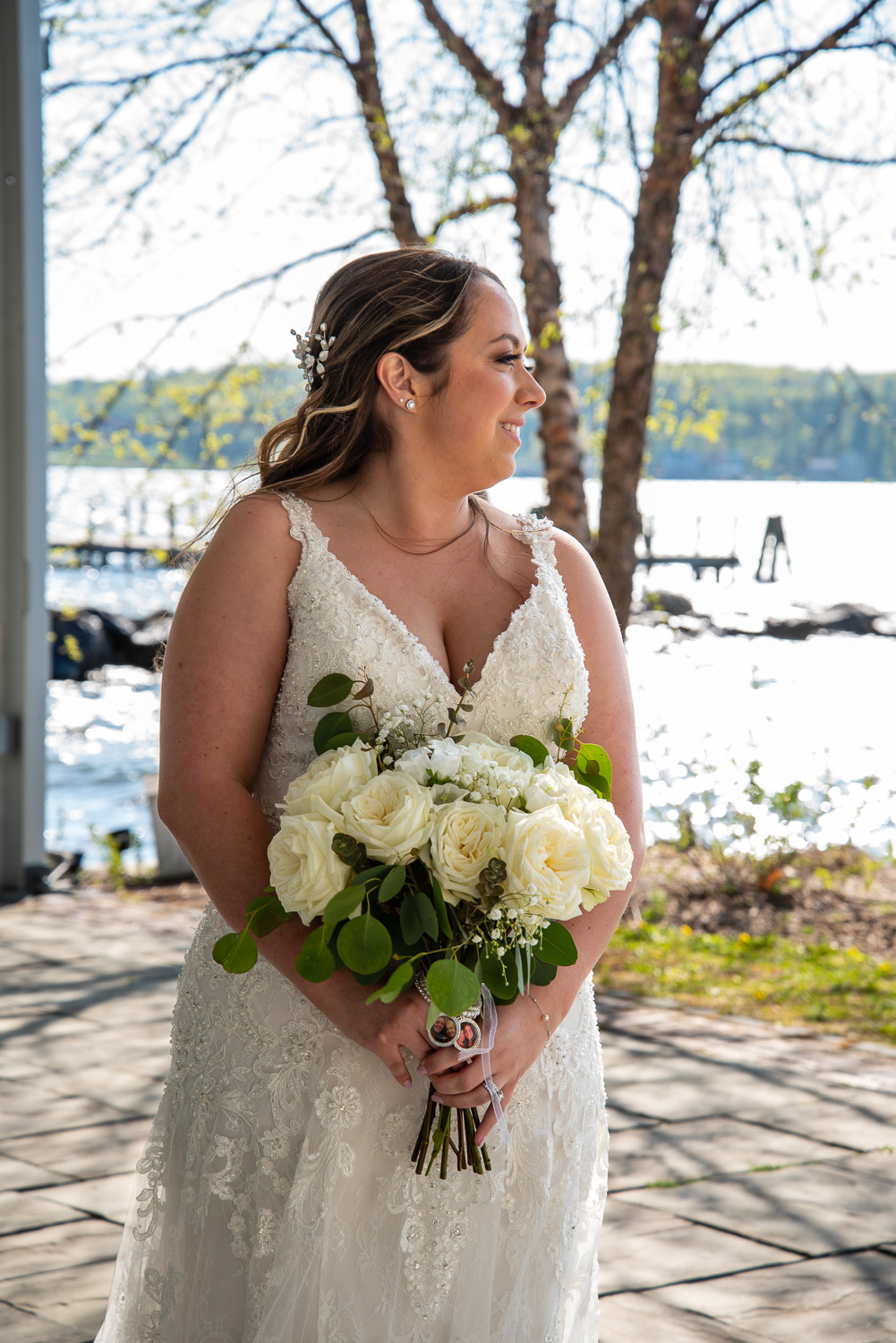 Bride looking to her left holding her bouquet with the lake behind her at the lakeside wedding