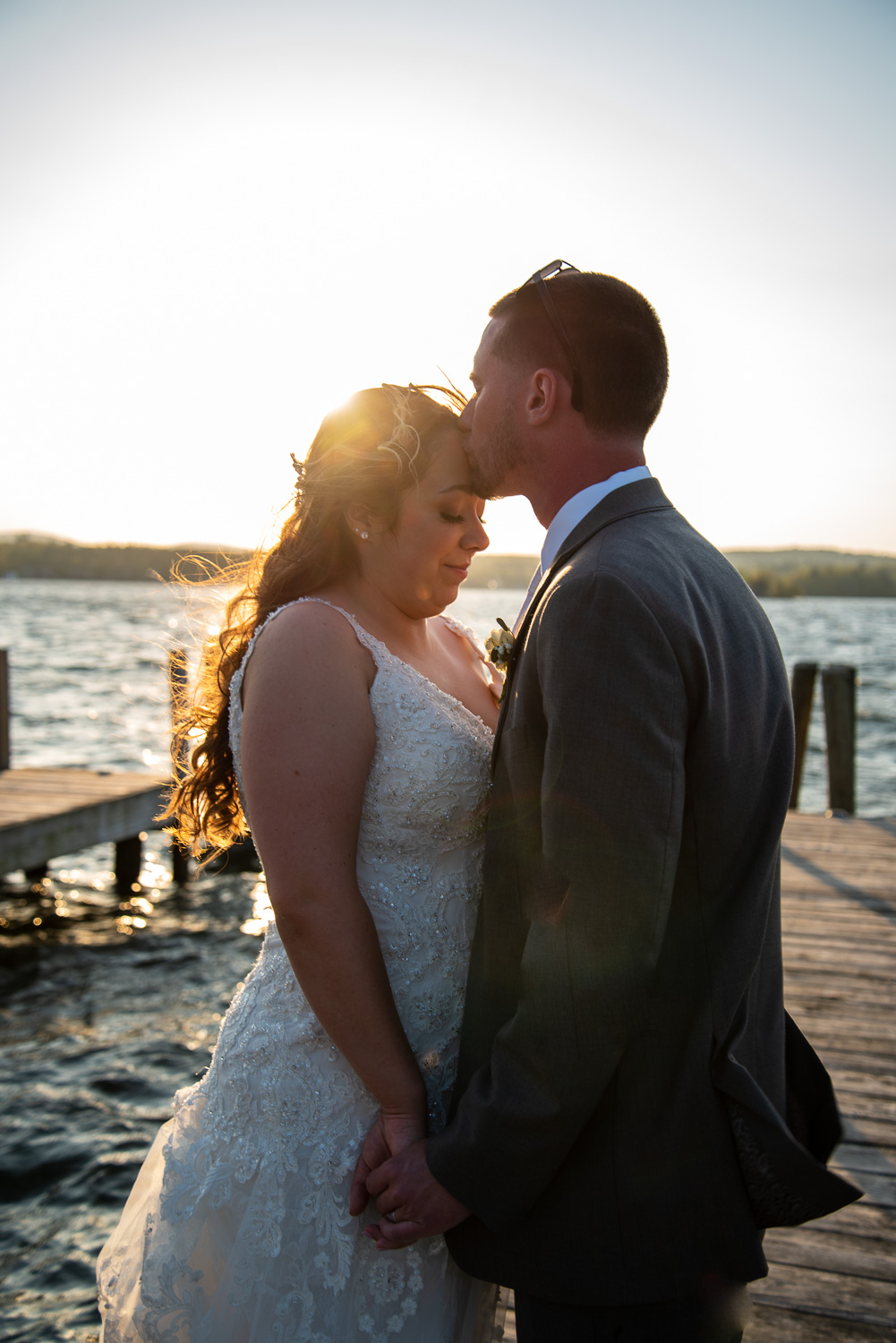 Bride and groom standing on a dock with the sun setting at the lakeside wedding