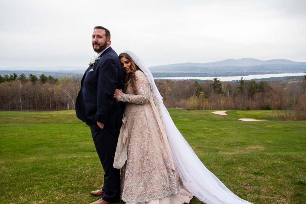 bride and groom smiling at each other at their wedding with a view with the mountains and lakes of NH behind them