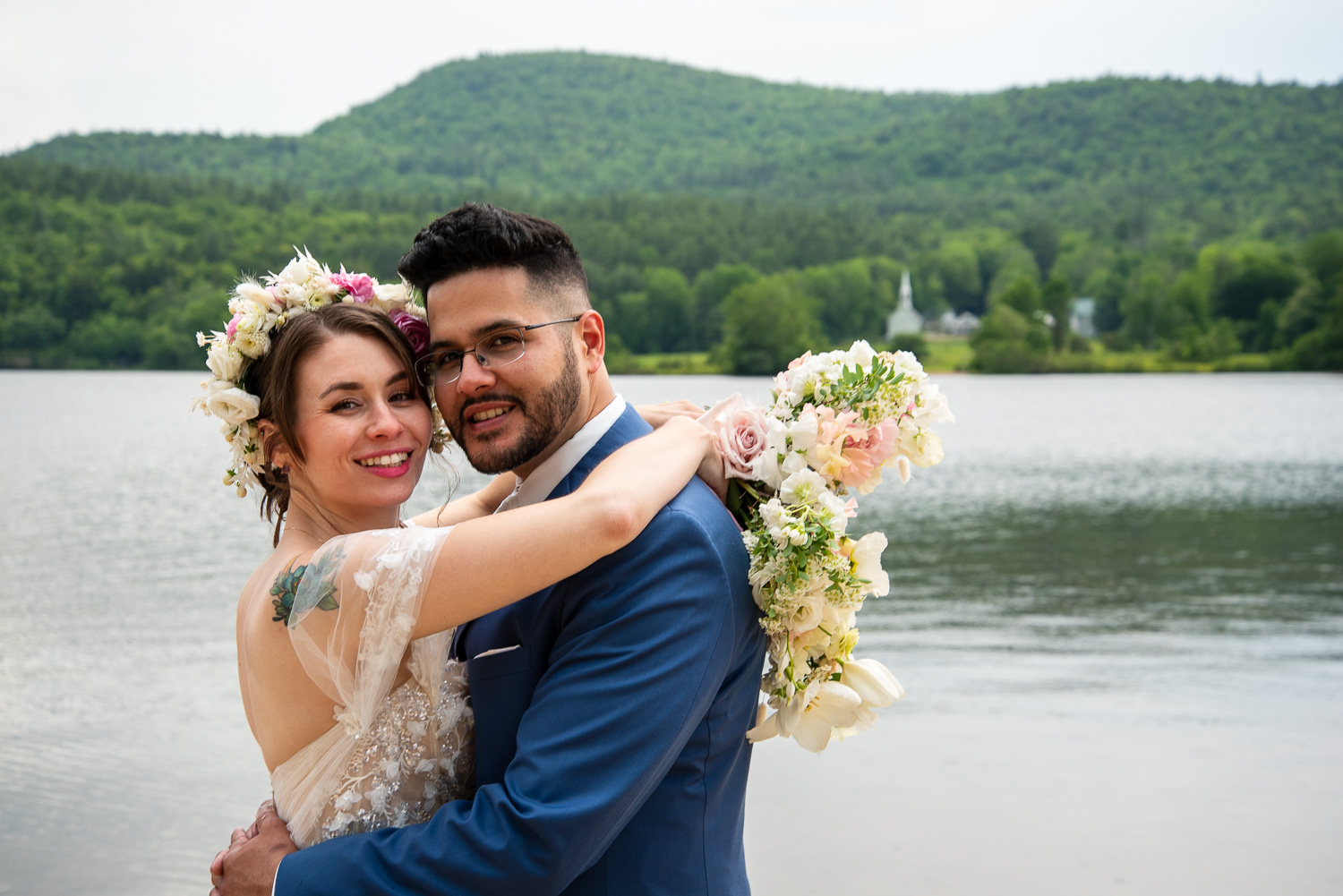 The Bride hugging the groom with the lake and little white church in the background on the sweetest wedding day