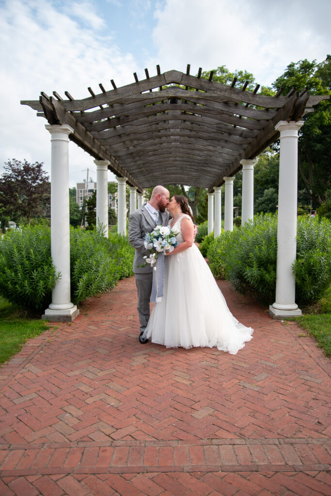 The bride and groom kissing under the archway at the coastal wedding