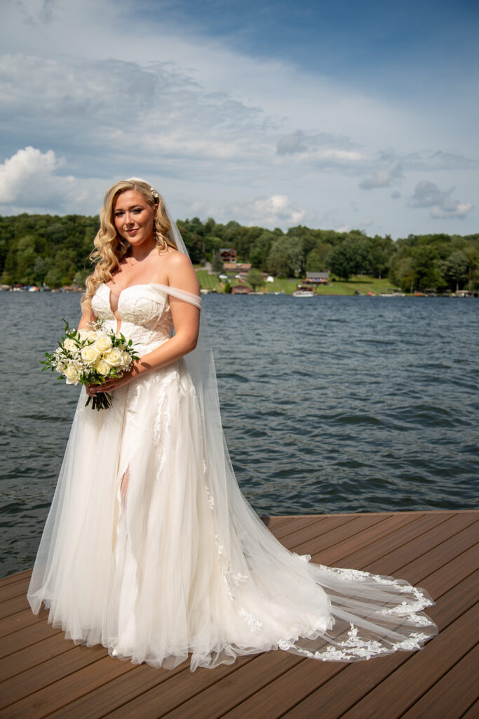 Bride with her bouquet in her hands and the lake behind her before her summer getaway wedding