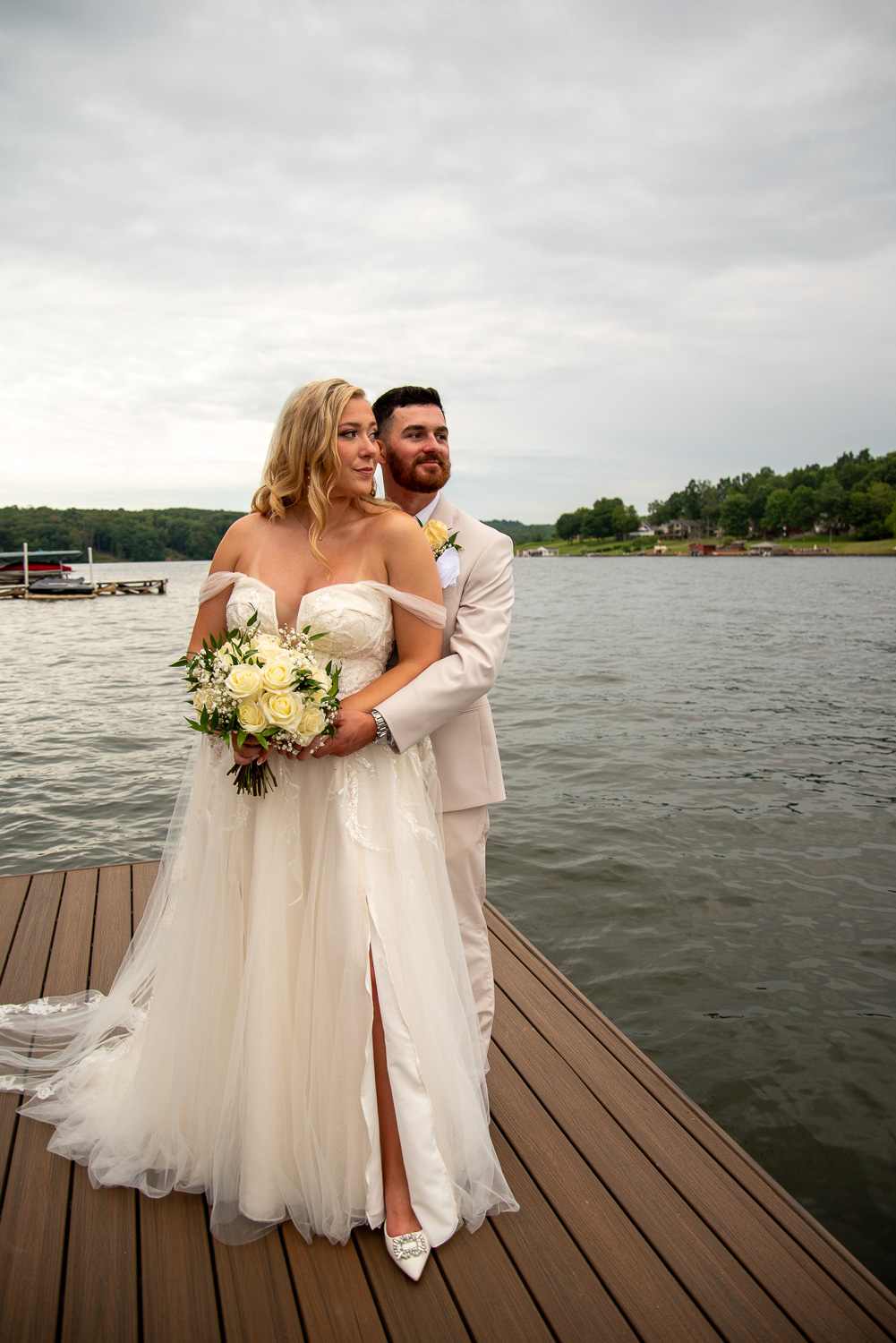 The bride and groom standing on a dock with the lake behind them after the summer getaway wedding