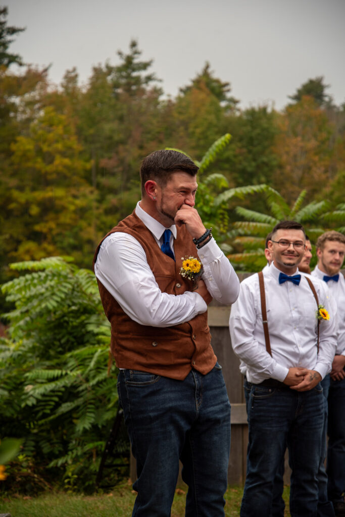 The groom getting emotional as the bride walks down the aisle toward him during the rustic fall wedding,