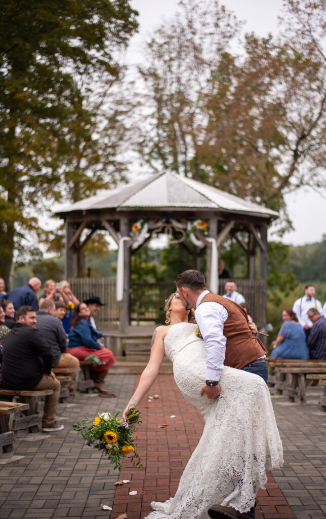 The groom dipping the bride and kissing her as they walk back down the aisle leaving the ceremony of the rustic fall wedding.