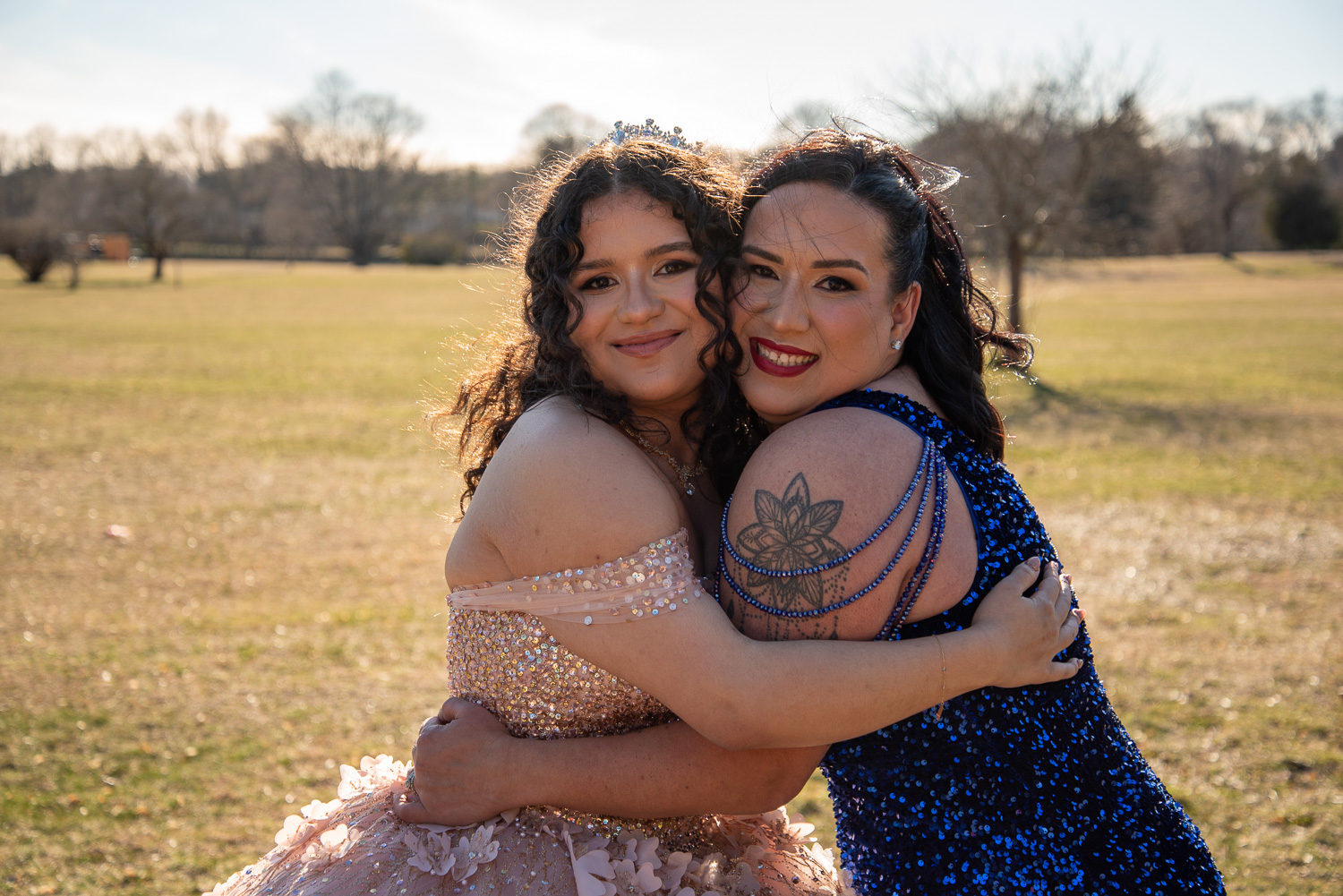 Beautiful sweet 16 birthday girl in her light pink ballgown posing at the park with her mom hugging her