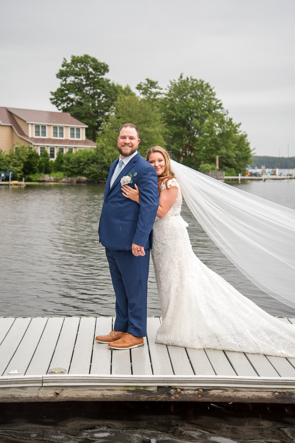 The bride and groom on the dock with the lake behind them after the rainy lakeside wedding